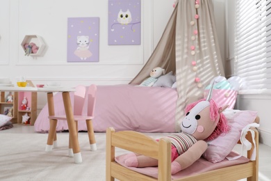 Photo of Cute toy unicorn on small bed in playroom, space for text. Interior design