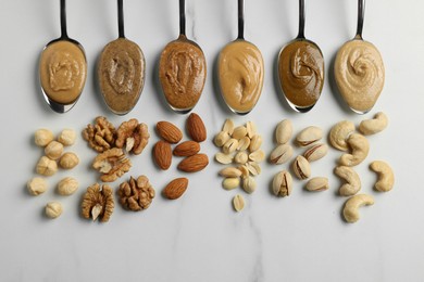 Tasty nut butters in spoons and raw nuts on white marble table, flat lay