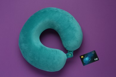 Photo of Turquoise travel pillow and credit card on purple background, flat lay