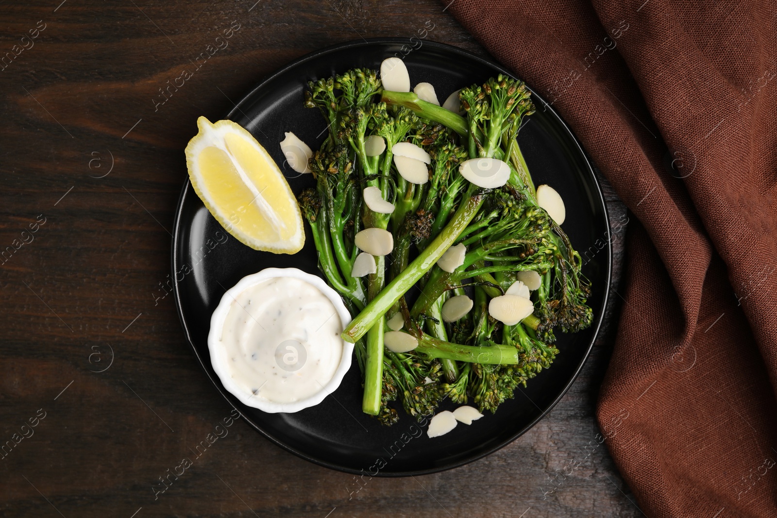 Photo of Tasty cooked broccolini with almonds, lemon and sauce on wooden table, top view