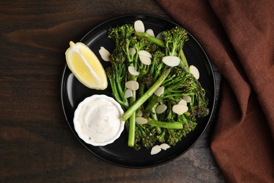 Photo of Tasty cooked broccolini with almonds, lemon and sauce on wooden table, top view