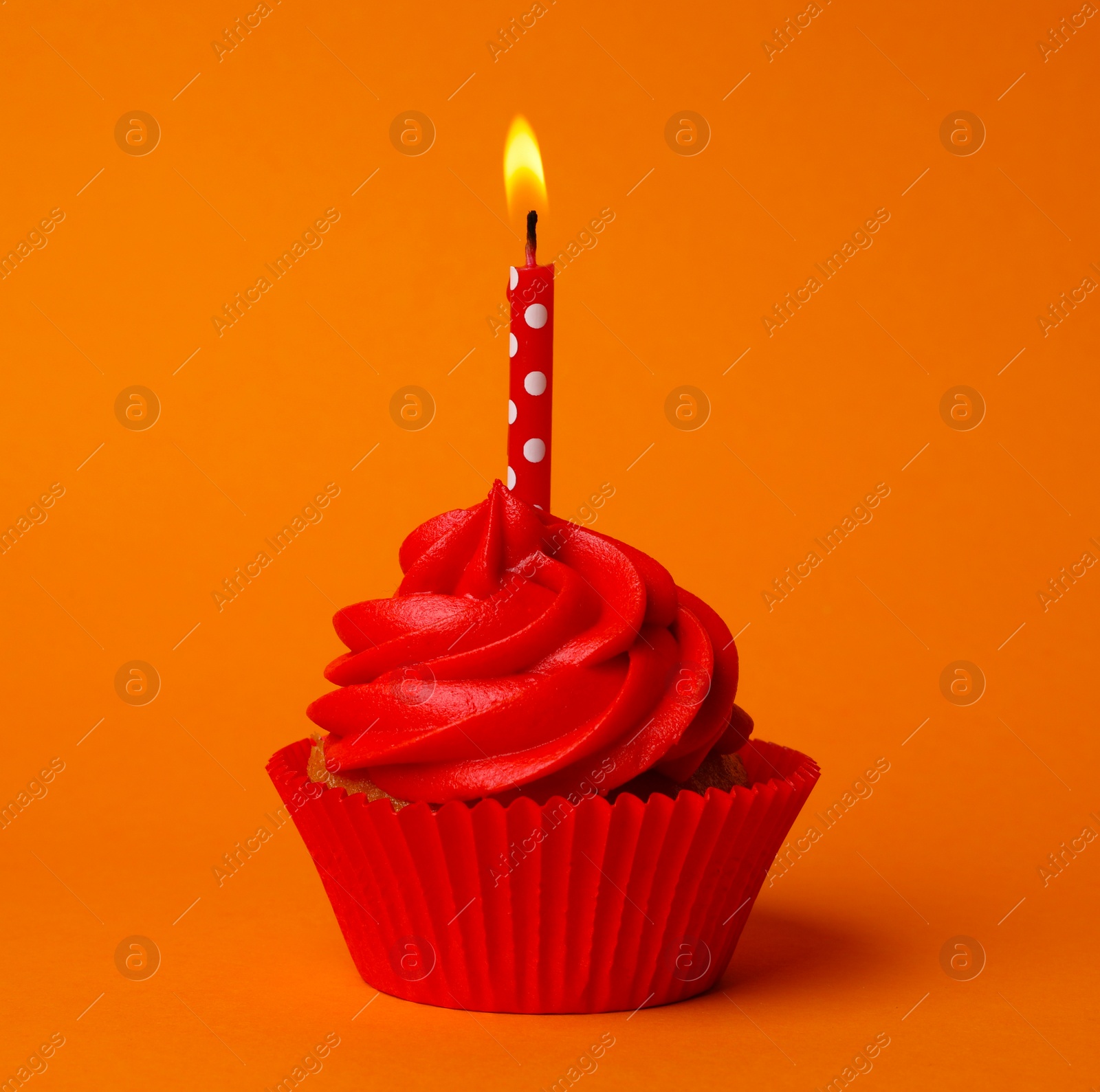 Photo of Delicious birthday cupcake with red cream and burning candle on orange background