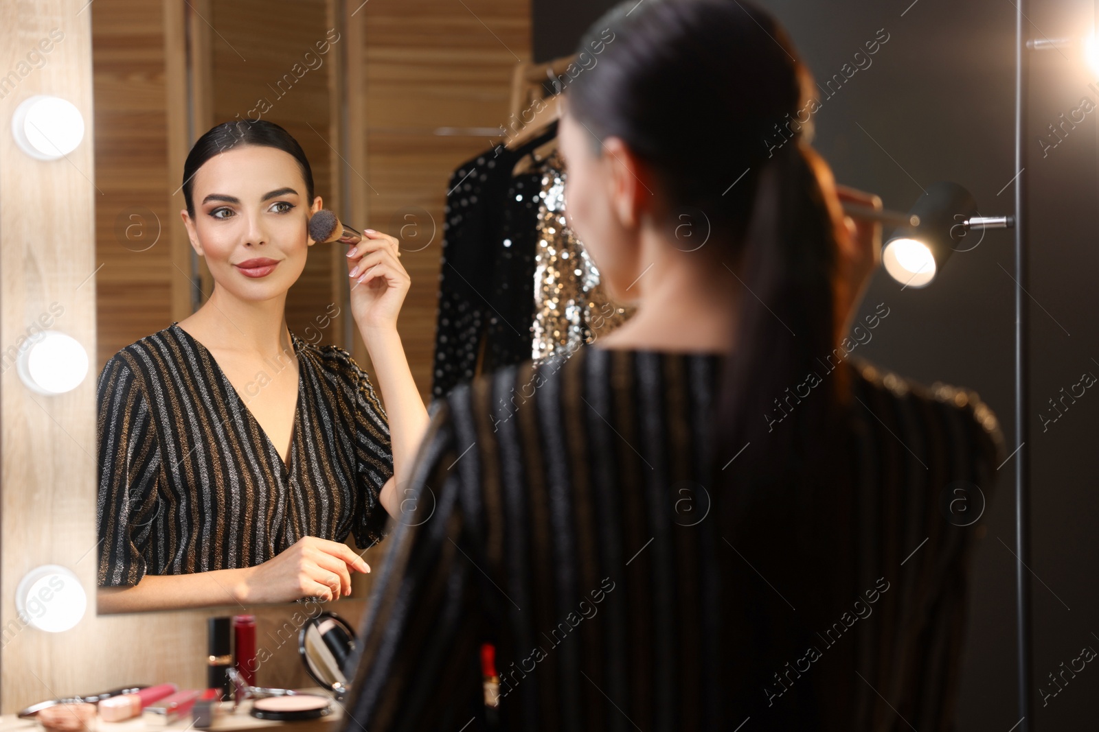 Photo of Bright makeup. Beautiful woman applying face powder near mirror in dressing room