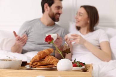 Photo of Tray with tasty breakfast in bed. Happy couple drinking coffee, selective focus