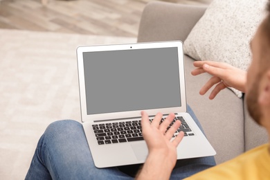 Photo of Young man using video chat on laptop in living room, closeup. Space for design