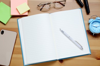 Photo of Empty notebook. smartphone, glasses and stationery on wooden table, flat lay