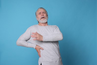 Senior man suffering from pain in back on light blue background, space for text. Arthritis symptoms
