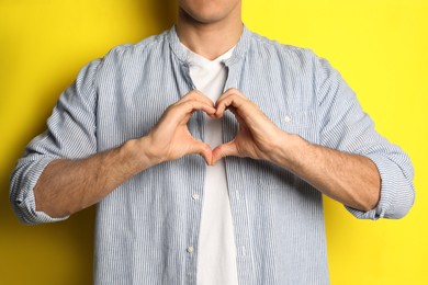 Photo of Man making heart with hands on yellow background, closeup
