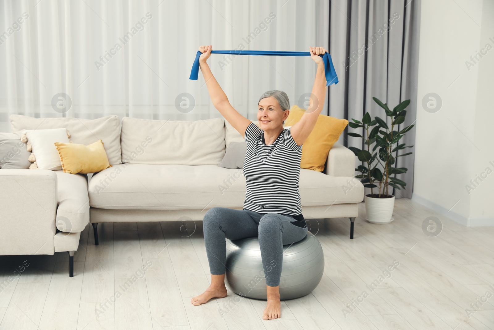 Photo of Senior woman doing exercise with elastic resistance band on fitness ball at home