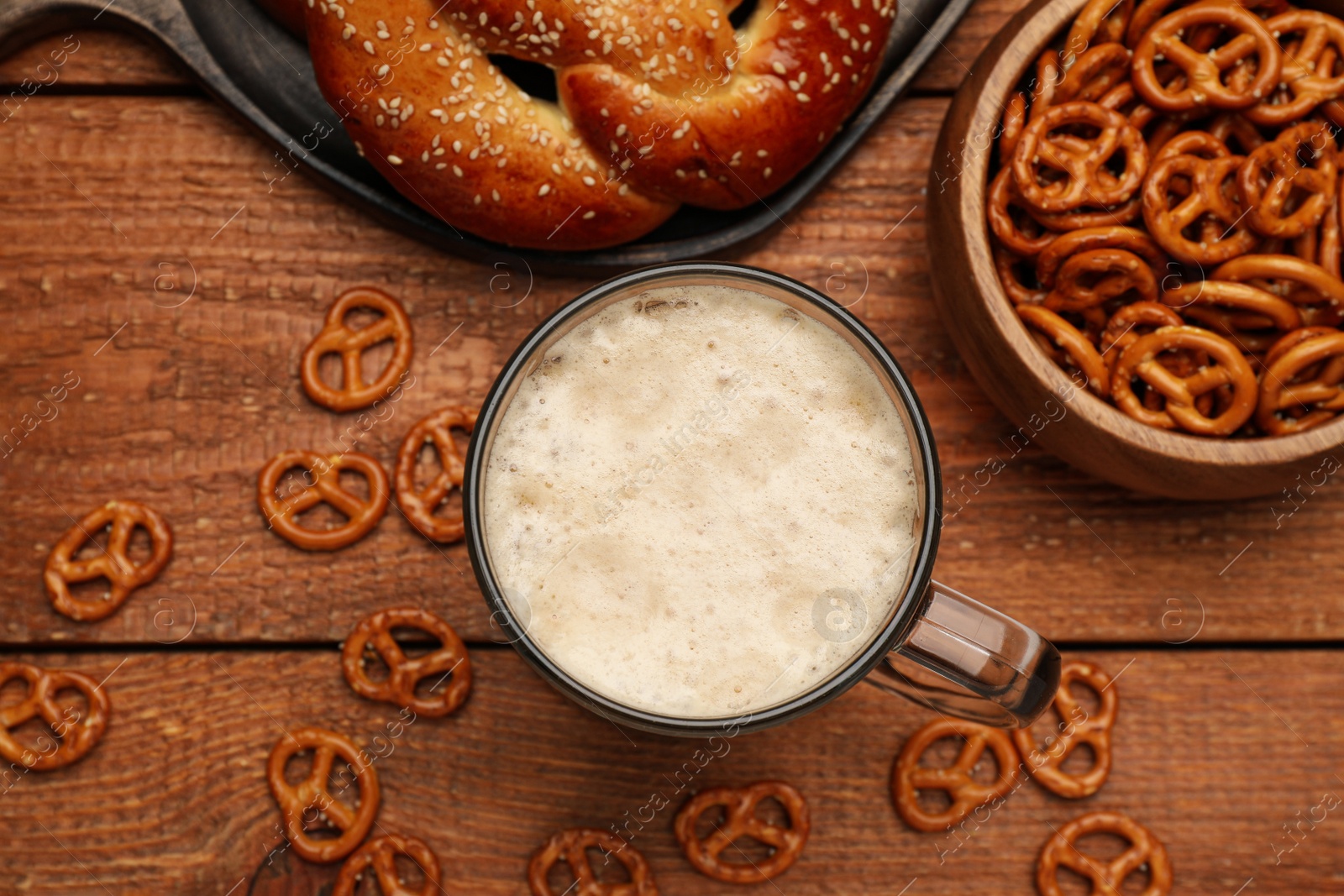 Photo of Tasty freshly baked pretzels, crackers and mug of beer on wooden table, flat lay