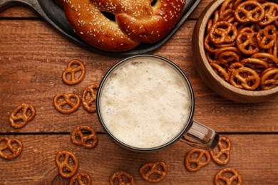 Tasty freshly baked pretzels, crackers and mug of beer on wooden table, flat lay