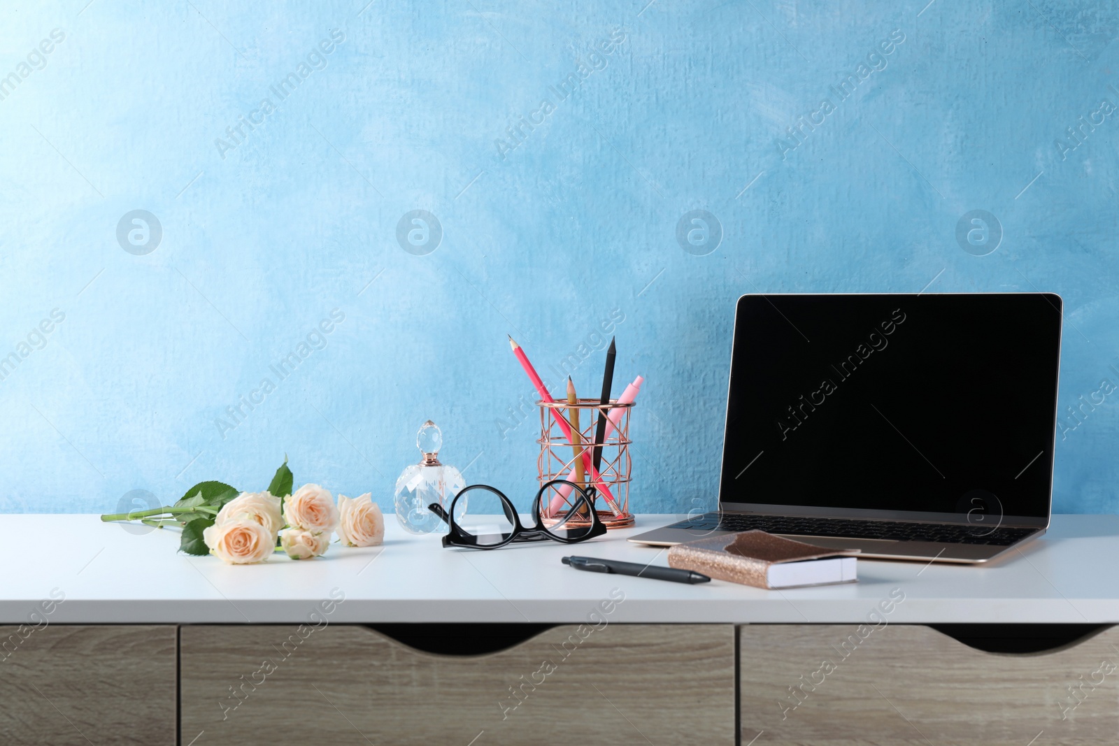 Photo of Comfortable workplace with modern laptop, stationery and flowers near light blue wall. Space for design