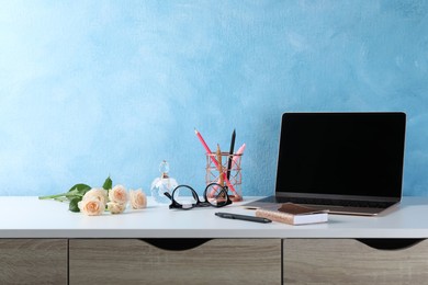 Photo of Comfortable workplace with modern laptop, stationery and flowers near light blue wall. Space for design