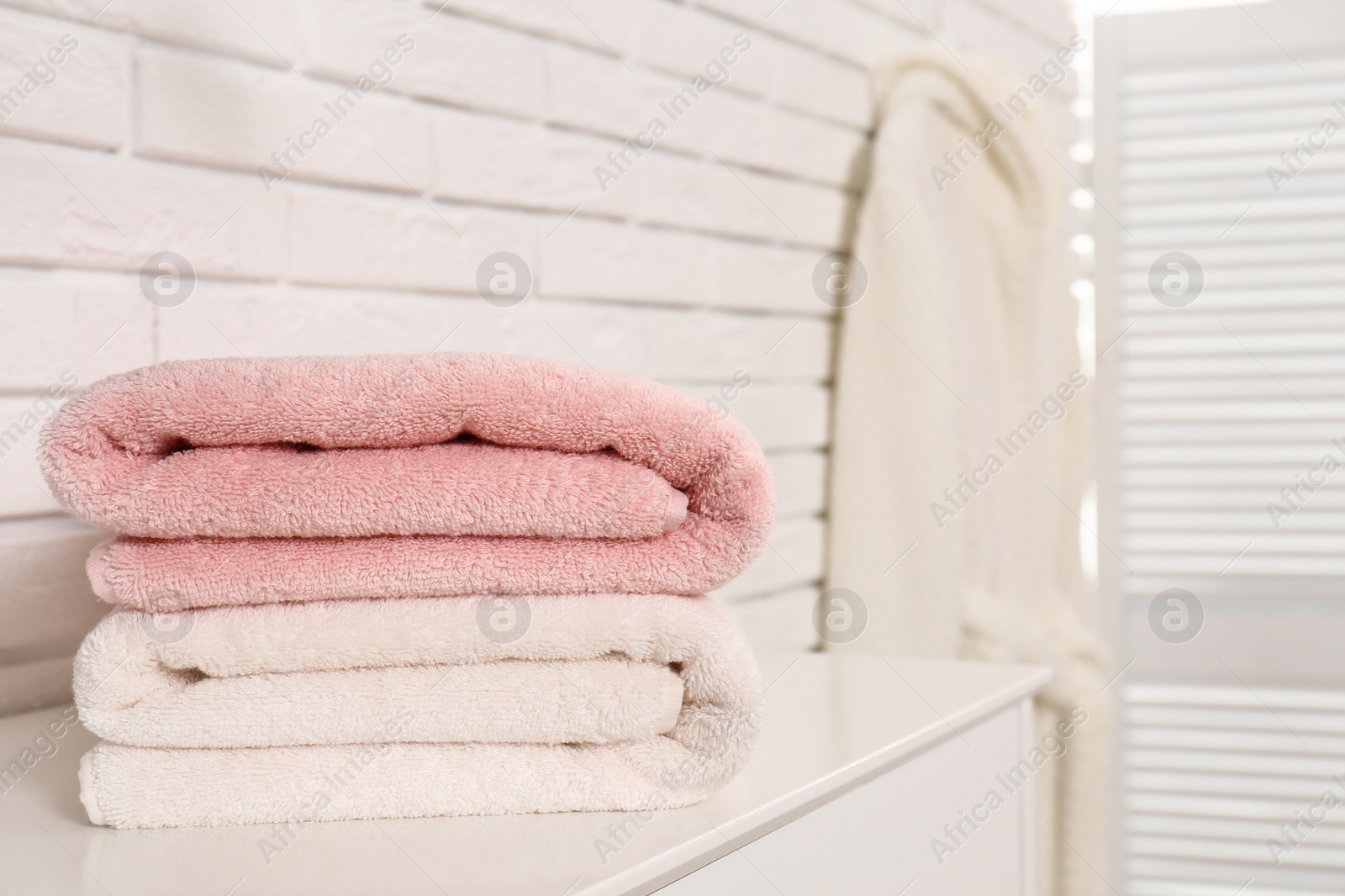 Photo of Clean folded towels on table near brick wall. Space for text