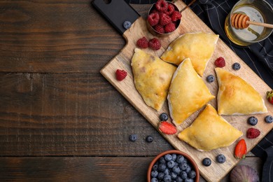 Photo of Delicious samosas, berries and honey on wooden table, flat lay. Space for text
