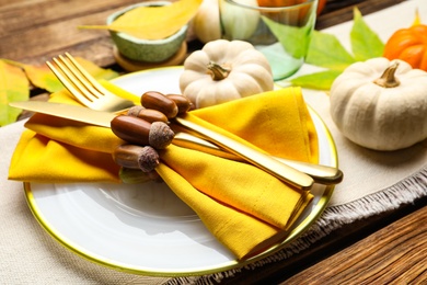 Seasonal table setting with acorns and other autumn decor on wooden background, closeup