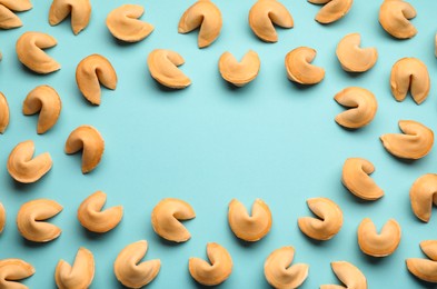 Frame of tasty fortune cookies with predictions on light blue background, flat lay. Space for text