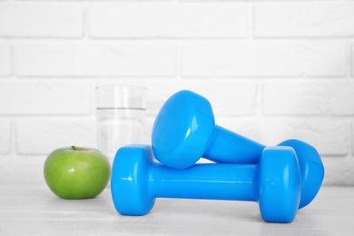 Photo of Stylish dumbbells, apple and glass of water on table against brick wall, space for text. Home fitness