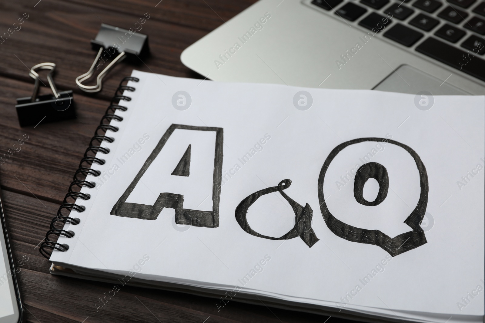 Photo of Notebook with text A&Q on wooden table, closeup