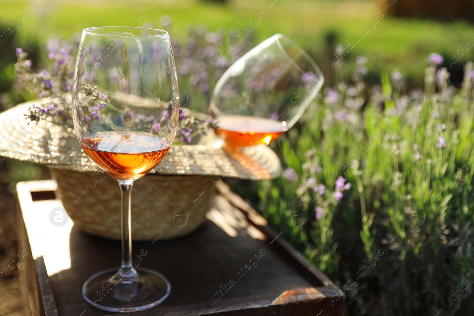 Photo of Straw hat and glasses of wine on wooden table in lavender field