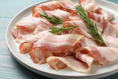 Slices of raw bacon and rosemary on light blue wooden table, closeup