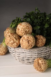Photo of Fresh raw celery roots in wicker basket on white wooden table