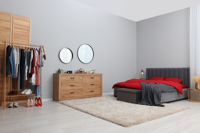 Photo of Stylish bedroom with comfortable bed, wooden chest of drawers and clothing rack. Interior design