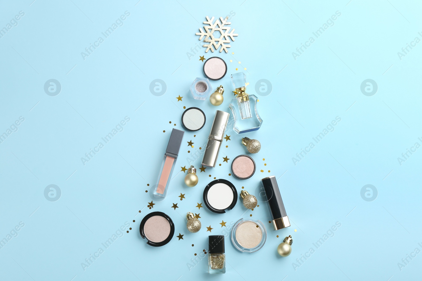 Photo of Christmas tree shape of decorative cosmetic products on light blue background, flat lay. Winter care