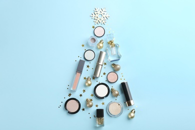 Photo of Christmas tree shape of decorative cosmetic products on light blue background, flat lay. Winter care