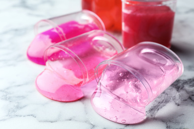 Photo of Overturned plastic containers with bright slimes on marble background, closeup