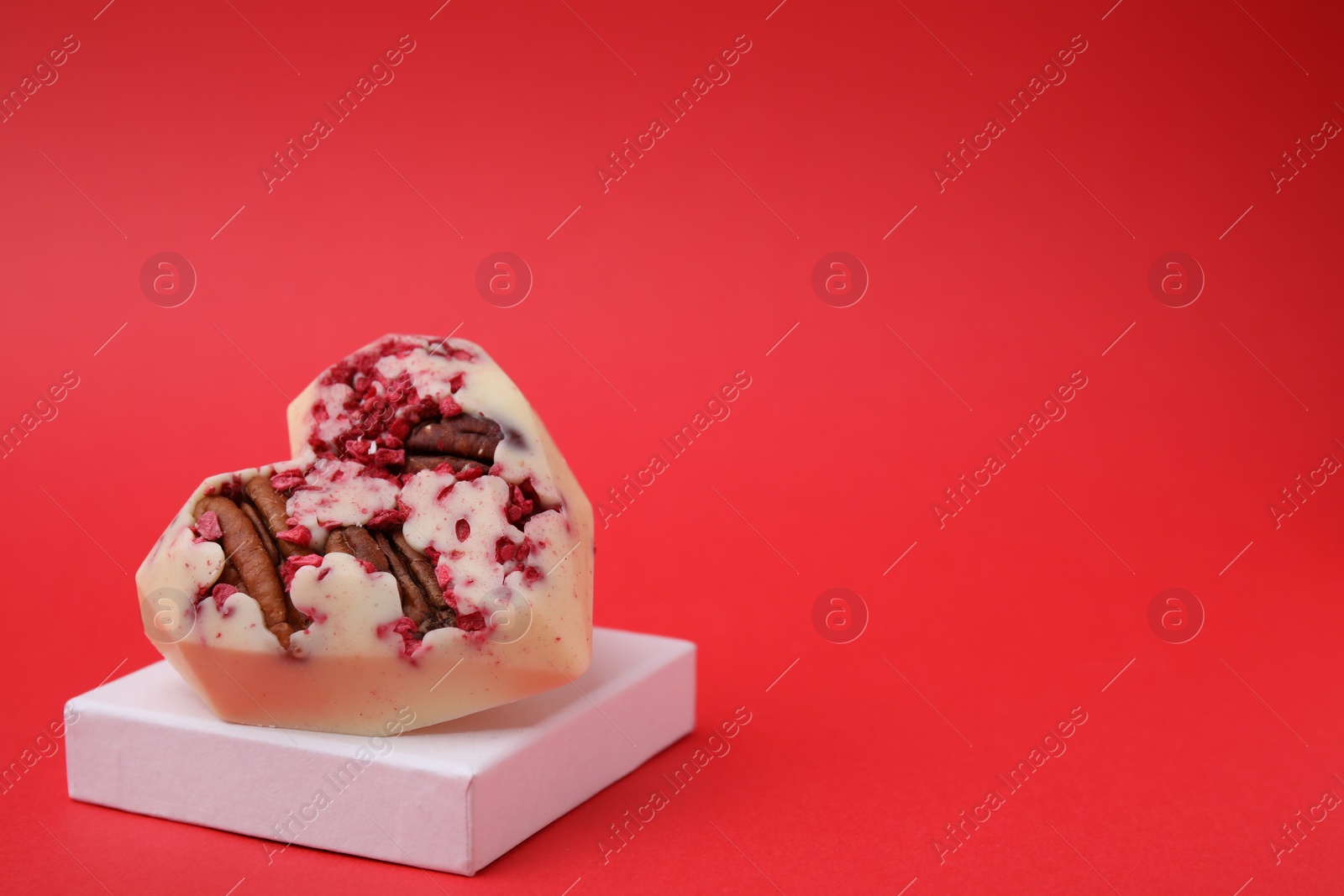 Photo of Tasty chocolate heart shaped candy with nuts on red background, space for text