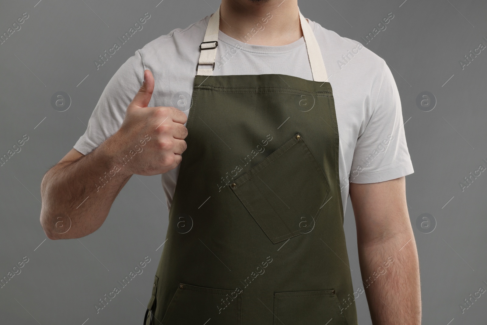 Photo of Man in kitchen apron showing thumb up on grey background, closeup. Mockup for design