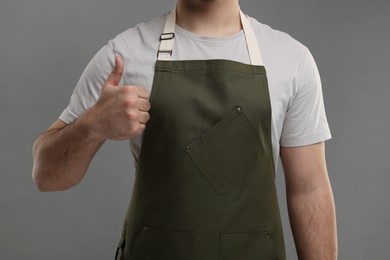 Man in kitchen apron showing thumb up on grey background, closeup. Mockup for design