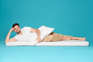 Photo of Man with pillow lying on soft mattress against light blue background