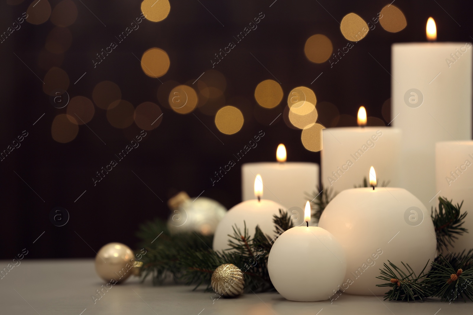Photo of Burning white candles with Christmas decor on table against blurred lights. Space for text