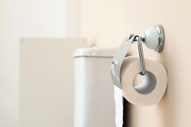 Photo of Holder with toilet paper roll on wall in bathroom. Space for text