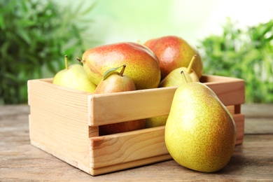 Photo of Crate with ripe juicy pears on brown wooden table against blurred background