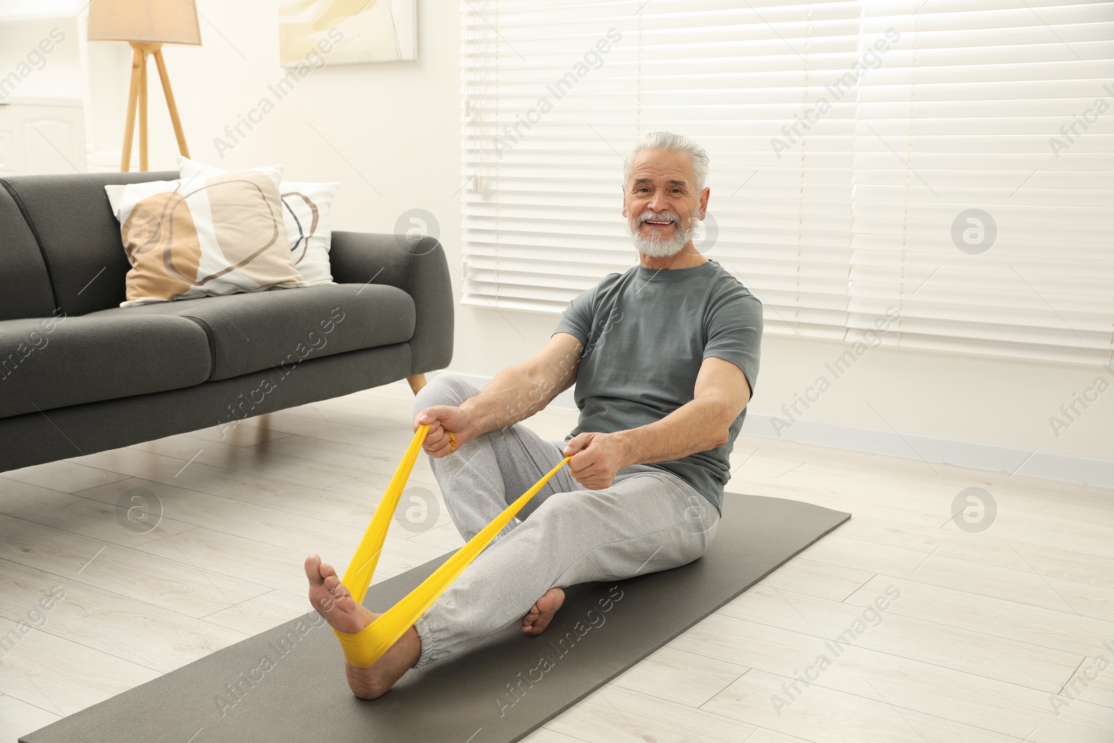 Photo of Senior man doing exercise with fitness elastic band on mat at home