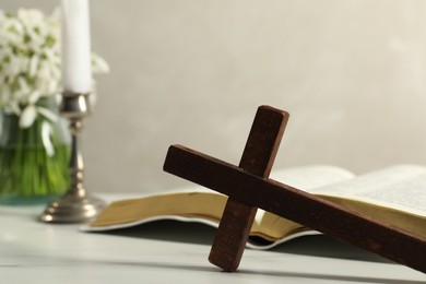 Photo of Wooden cross, Bible and church candle on white table, closeup