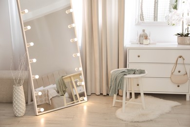 Photo of Large mirror with light bulbs and chest of drawers in stylish room. Interior design