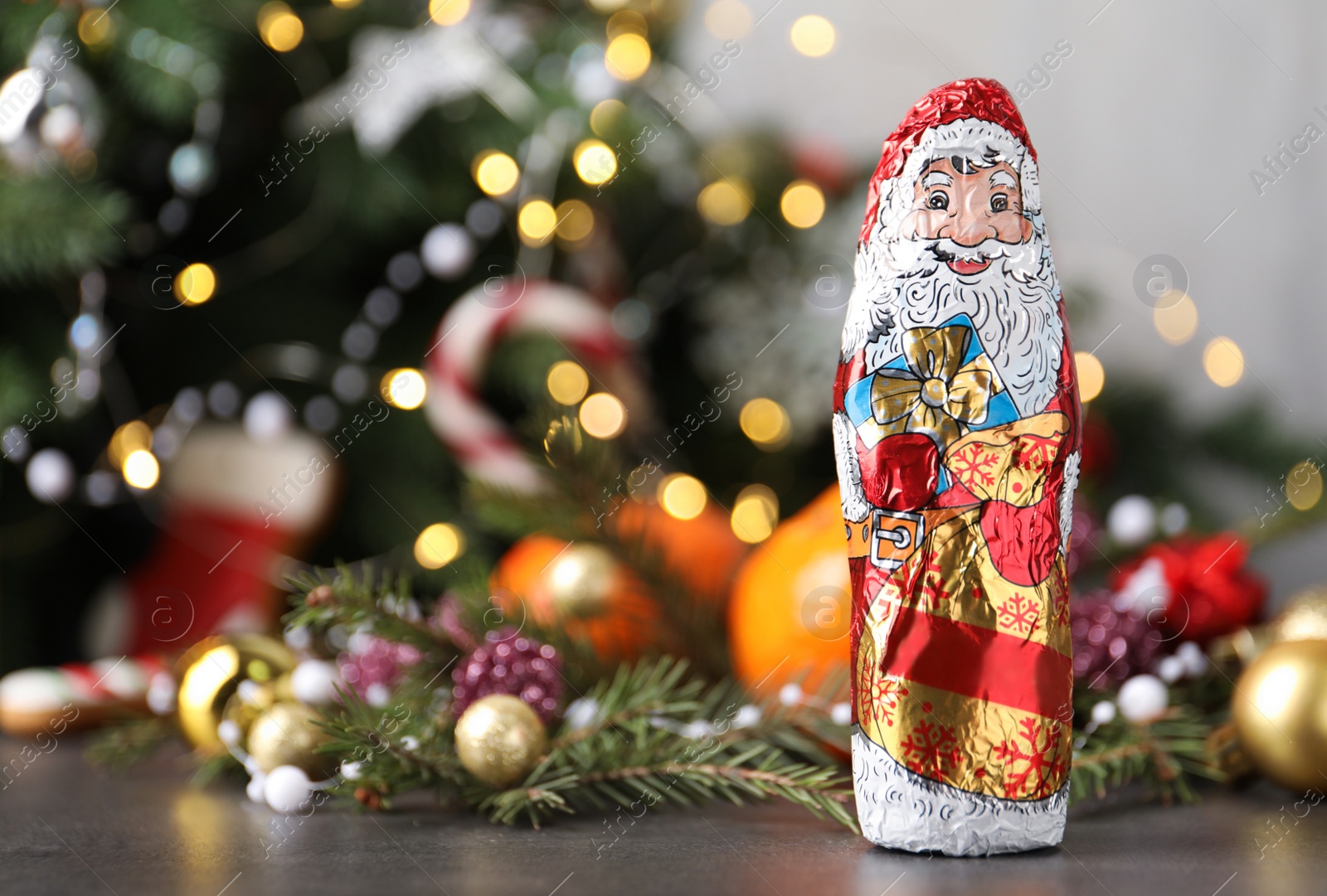 Photo of Chocolate Santa Claus and decorations on table near Christmas tree, space for text