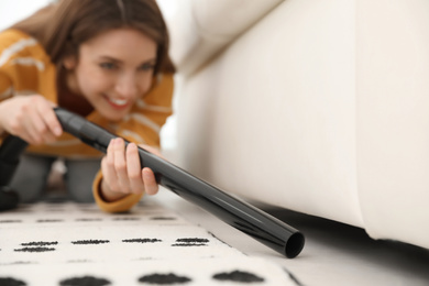 Photo of Young woman using vacuum cleaner at home