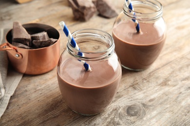 Photo of Jars with tasty chocolate milk on wooden table. Dairy drink