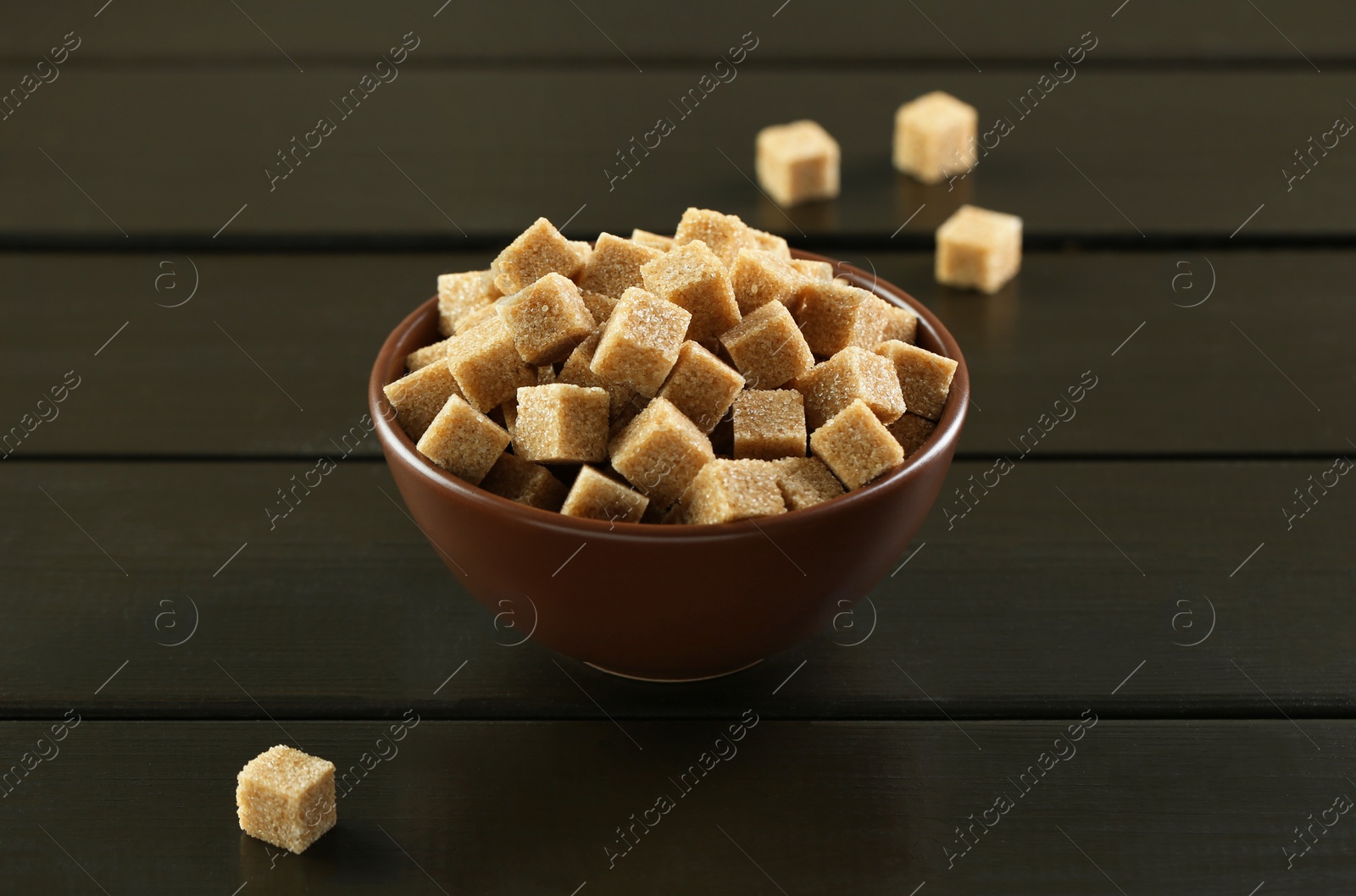 Photo of Brown sugar cubes in bowl on black wooden table