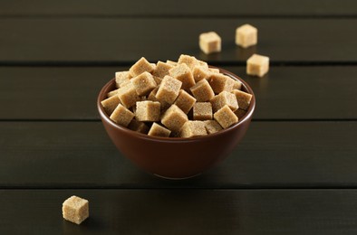 Photo of Brown sugar cubes in bowl on black wooden table