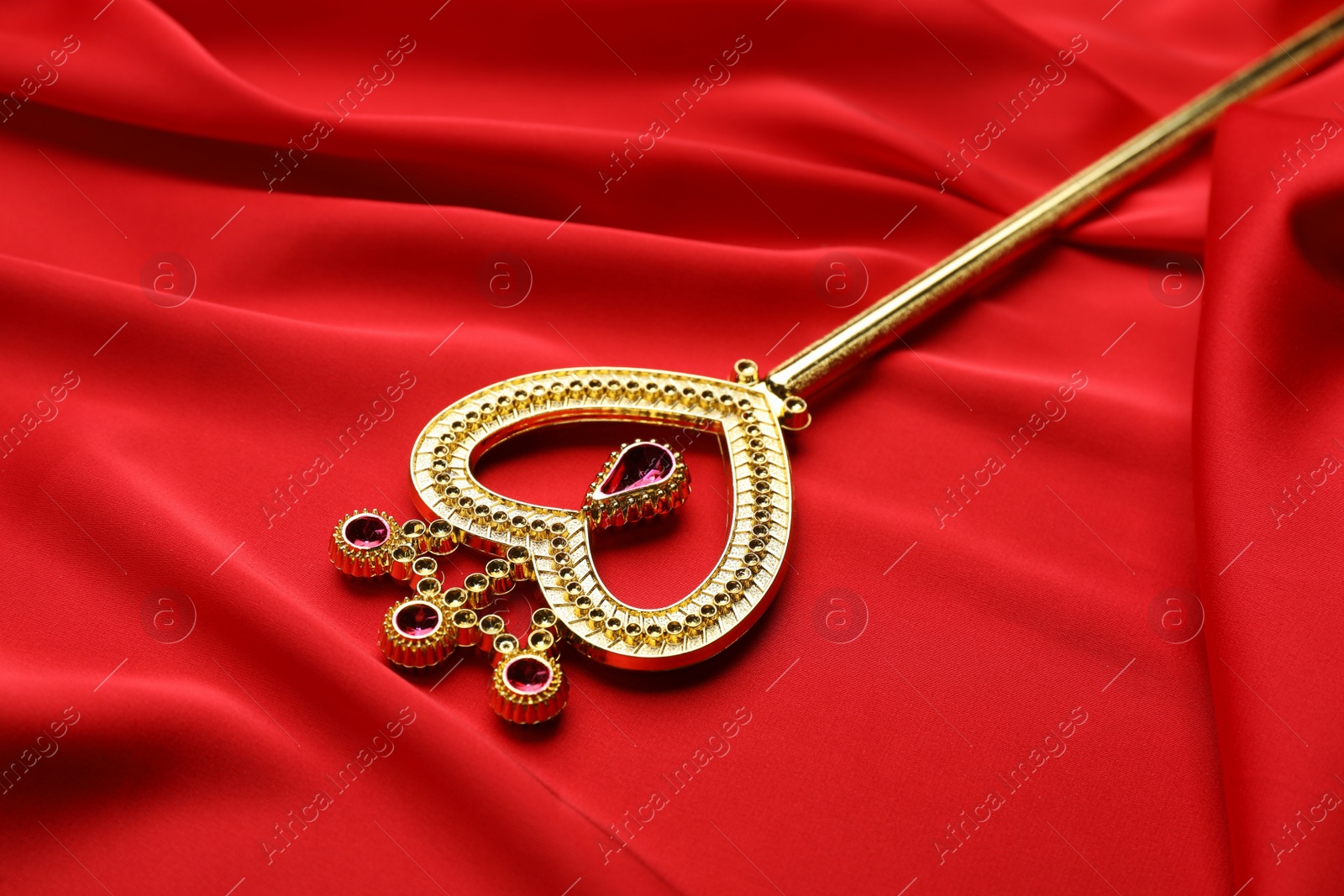 Photo of Beautiful golden magic wand on red fabric, closeup