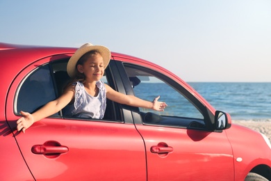 Photo of Happy little girl leaning out of car window on beach. Summer trip