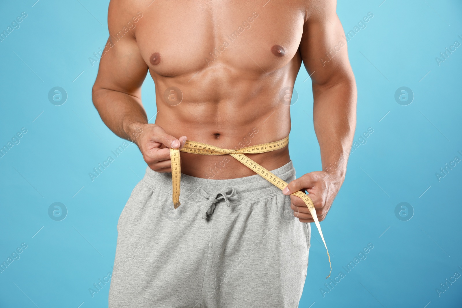 Photo of Young man with slim body using measuring tape on light blue background, closeup view