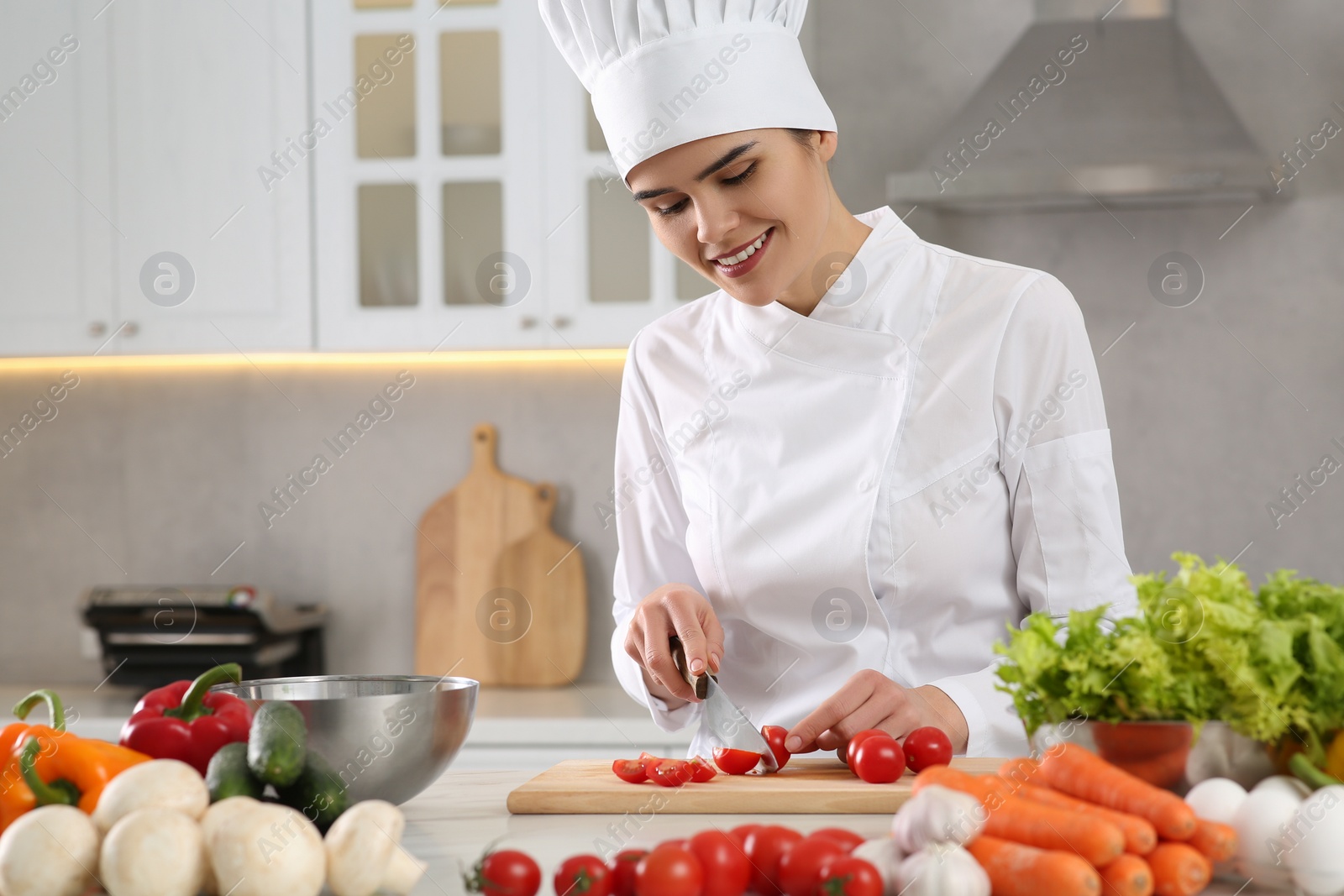 Photo of Professional chef cutting fresh tomatoes at white table in kitchen