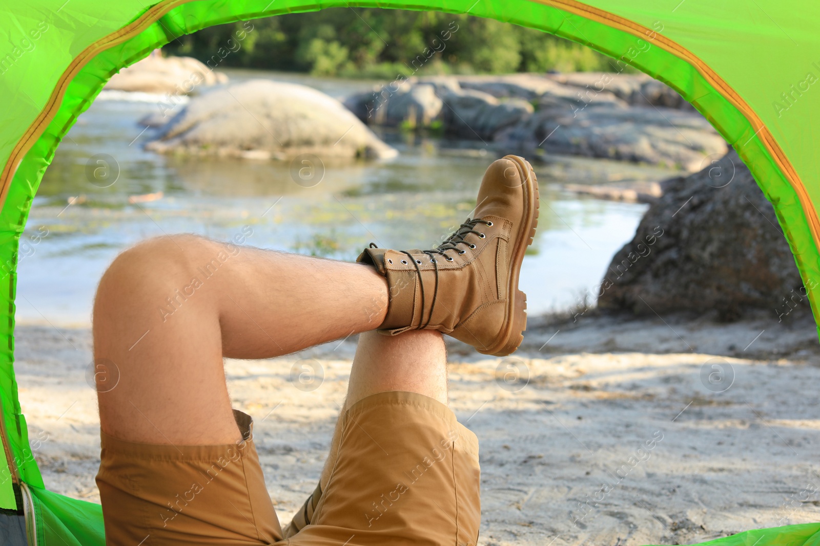 Photo of Young man resting in camping tent on riverbank, view from inside